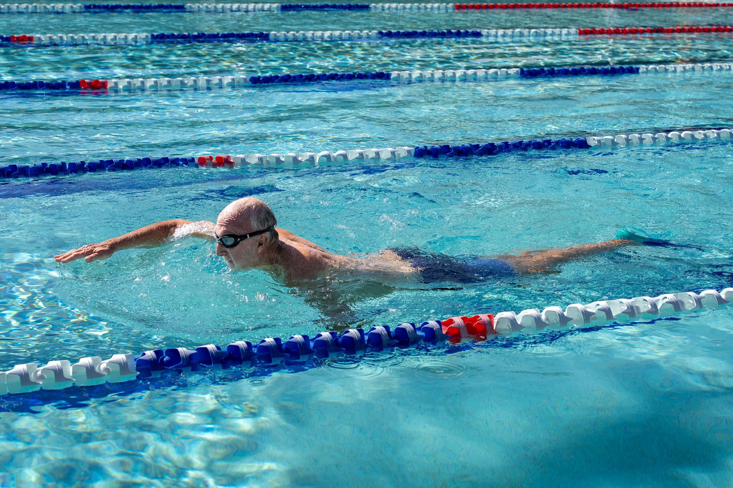 Older gentleman swims laps in outdoor pool.